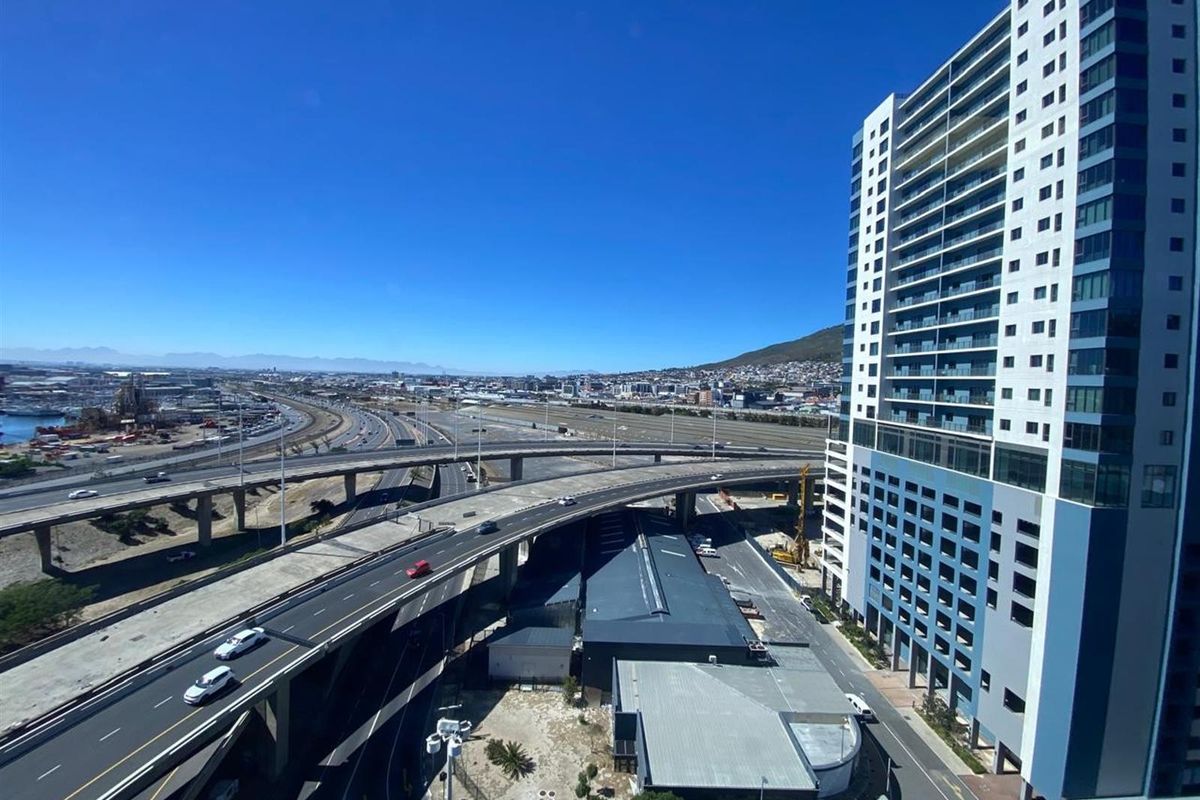 Elevated aerial view showcasing the surrounding urban infrastructure, major highway interchanges, and the adjacent high-rise office building.