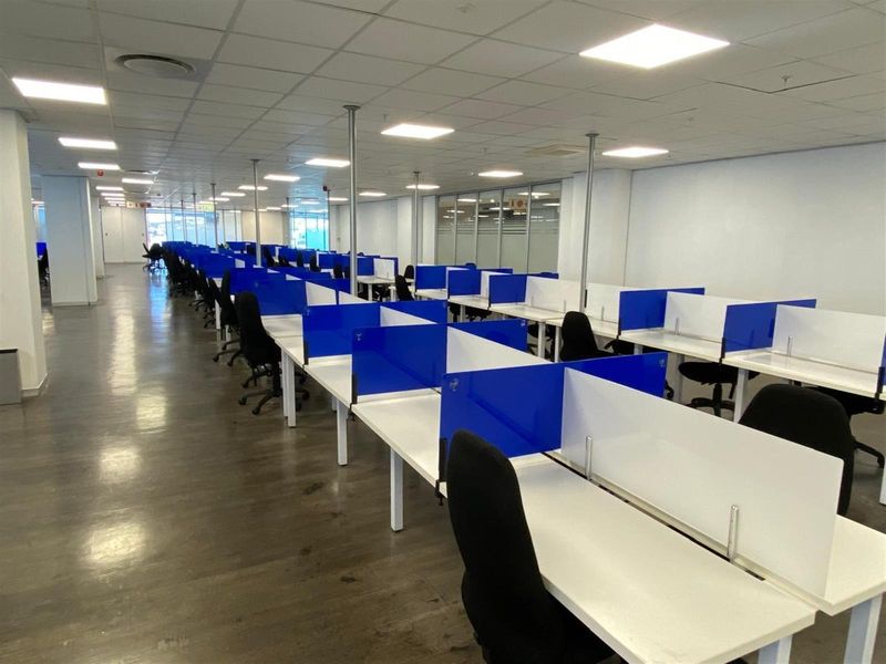 Open-plan office space featuring rows of modular workstations with privacy screens, suspended ceiling tiles, and recessed lighting.