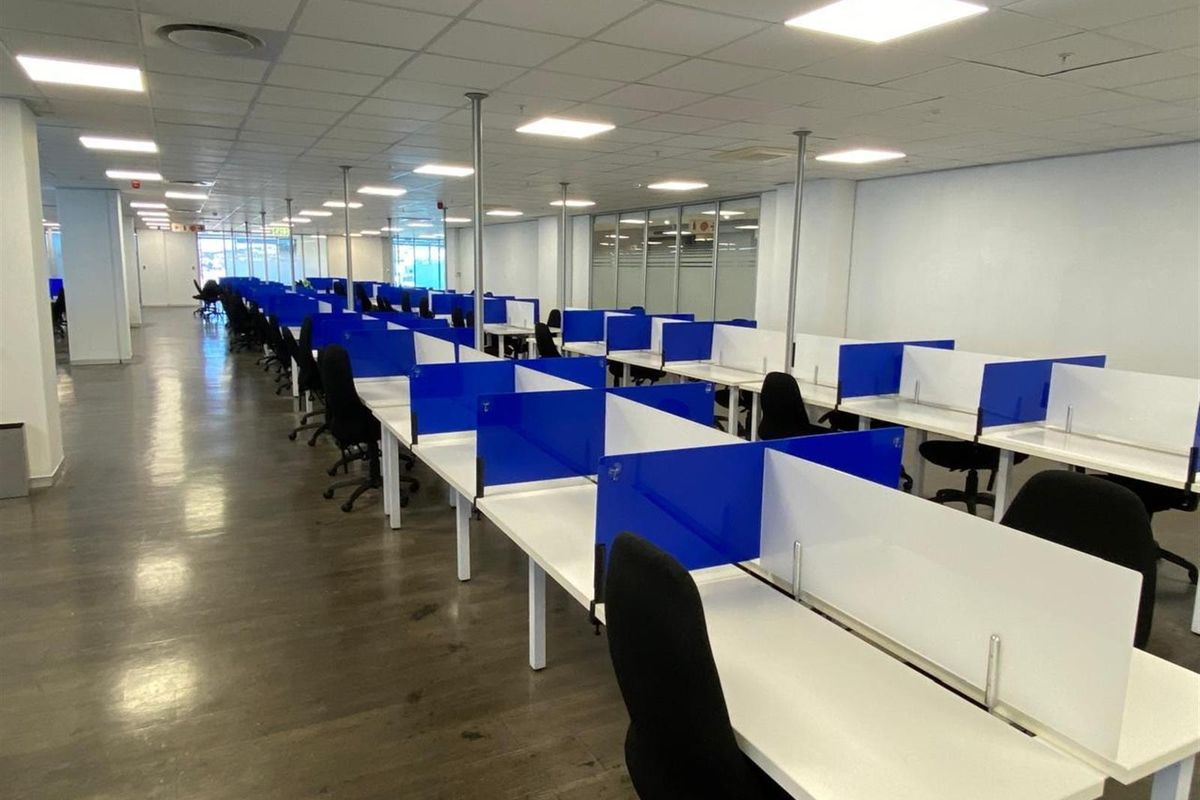 Open-plan office space featuring rows of modular workstations with privacy screens, suspended ceiling tiles, and recessed lighting.
