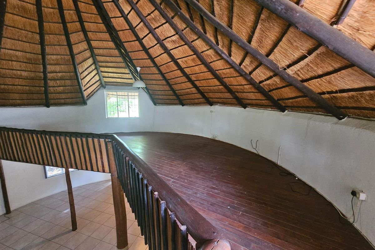 A mezzanine loft area featuring a high thatched roof, timber flooring, and a wooden balustrade overlooking the lower level.