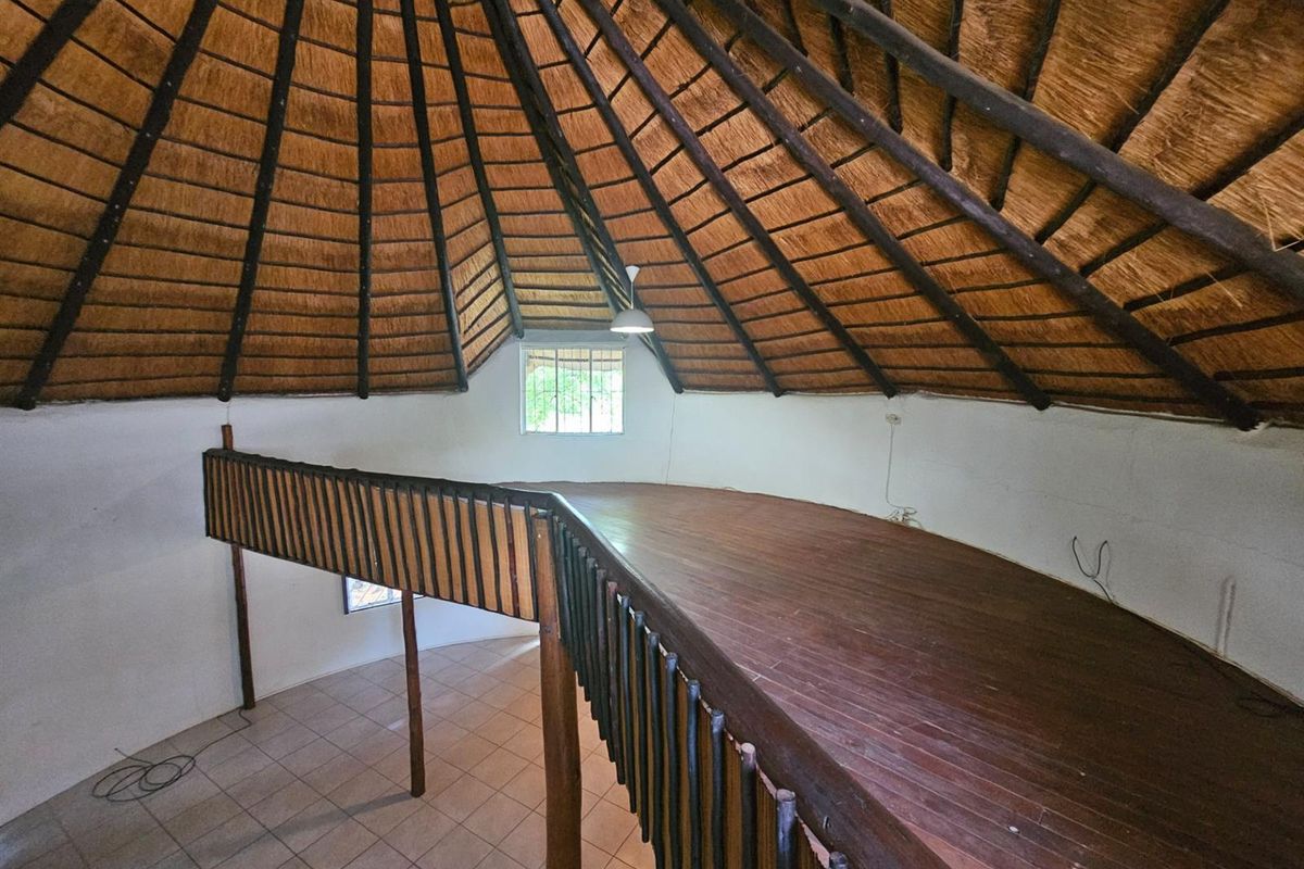 A unique mezzanine level featuring a high thatched roof, timber flooring, and a wooden balustrade overlooking the lower living area.