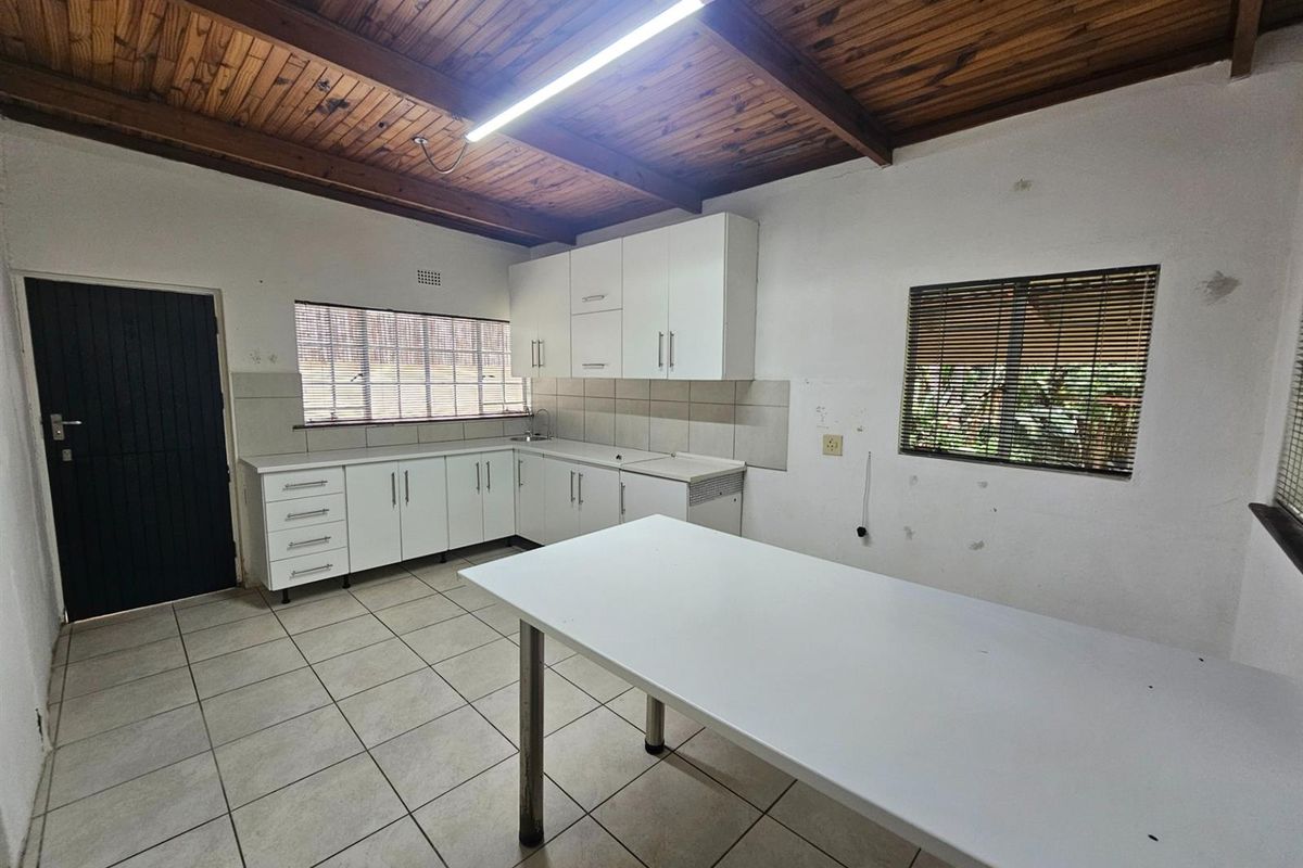 A functional kitchen featuring white cabinetry, tiled flooring, and a timber-paneled ceiling, providing a practical workspace with ample storage and natural light.