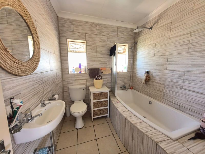 A functional bathroom featuring a built-in bathtub with shower mixer, wall-mounted basin, and toilet, finished with neutral textured wall tiles.
