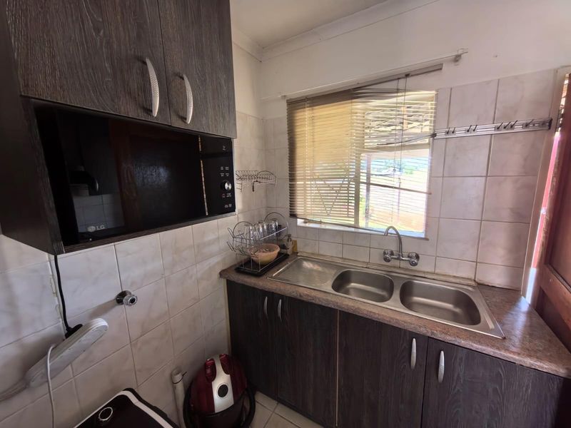 A functional kitchen area featuring dark wood-grain cabinetry, a double stainless steel sink, and tiled splashbacks.