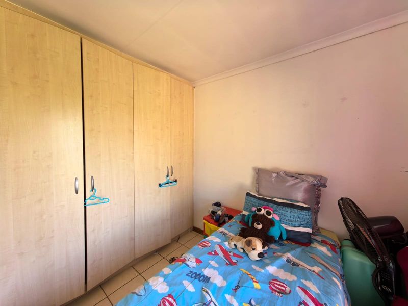 A bedroom featuring built-in light wood-finish cupboards and tiled flooring.