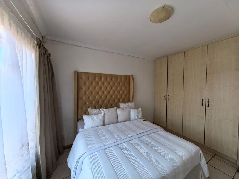 A bedroom featuring built-in wooden cabinetry and tiled flooring, offering a functional space with natural light from the adjacent window.