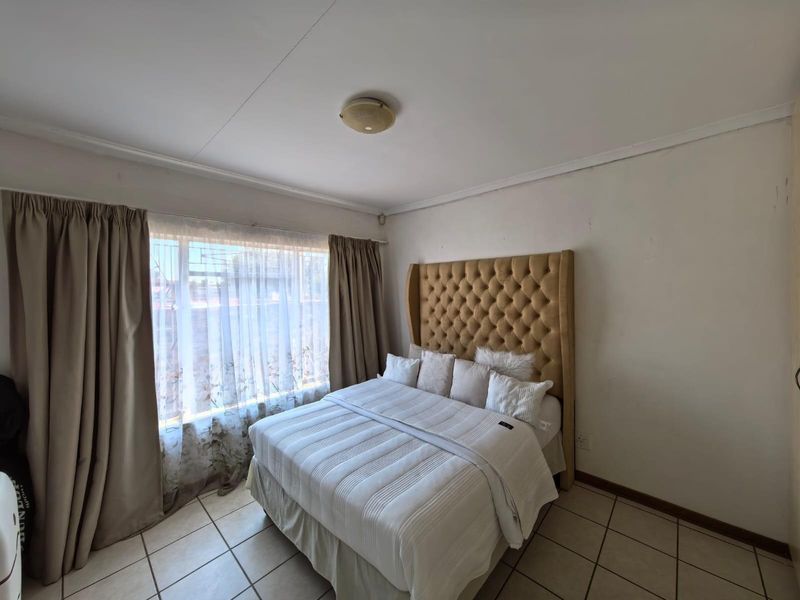 A bedroom featuring tiled flooring, a large window with curtain tracks, and a central ceiling light fixture.