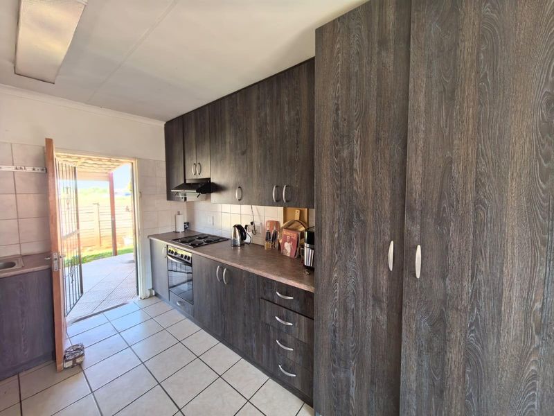 A functional kitchen featuring dark wood-grain cabinetry, built-in oven and hob, tiled flooring, and direct access to an outdoor patio area.