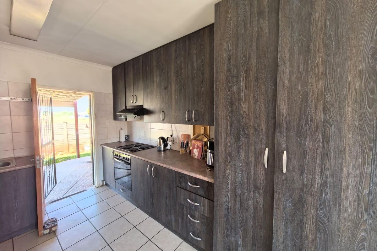 A functional kitchen featuring dark wood-grain cabinetry, built-in oven and hob, tiled flooring, and direct access to an outdoor patio area.