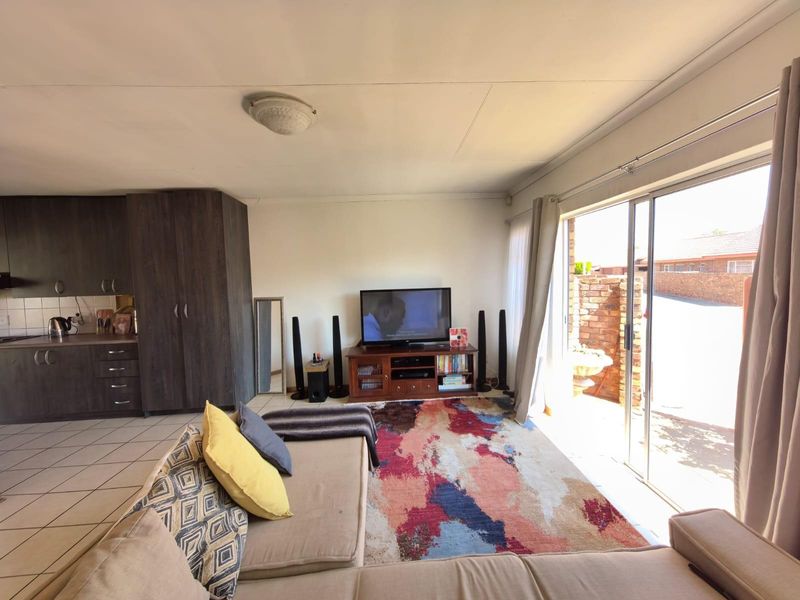 Open-plan living area featuring tiled flooring, a compact kitchen with dark cabinetry, and large sliding glass doors providing access to the exterior.