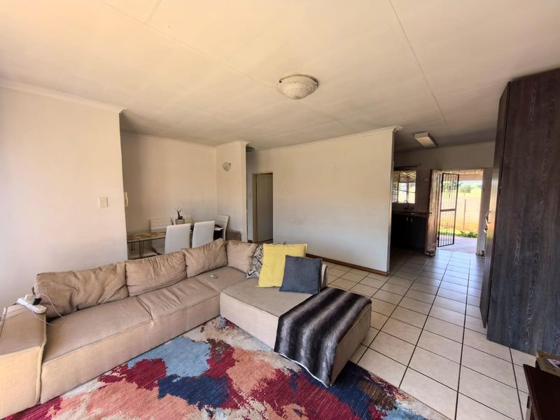 Open plan living and dining area featuring tiled flooring, leading towards a kitchen space with direct access to the exterior.