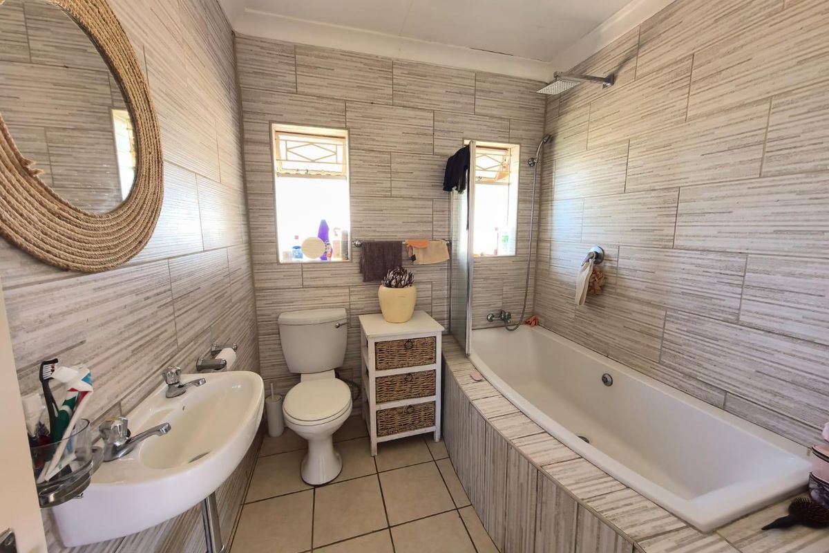 A functional bathroom featuring a built-in bathtub with shower mixer, wall-mounted basin, and toilet, finished with neutral textured wall tiles.