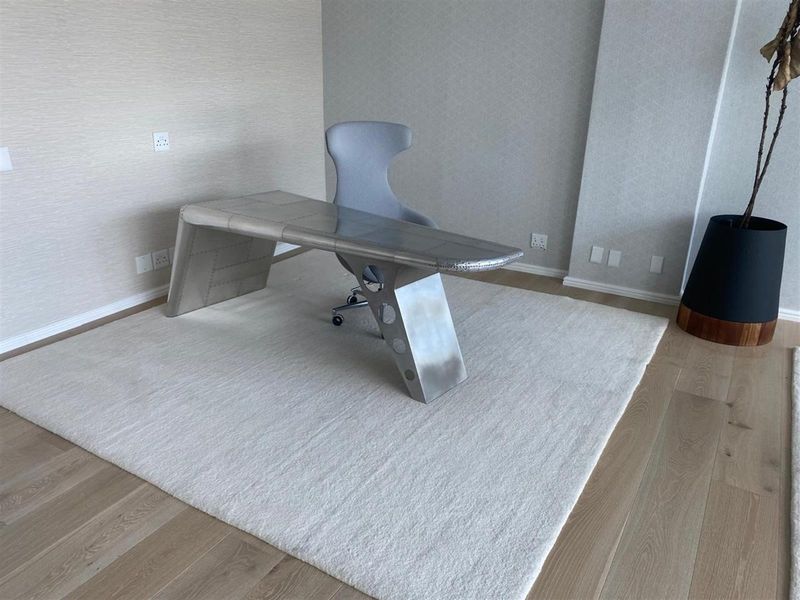 A modern office space featuring light hardwood flooring and neutral textured wallpaper, providing a clean and professional work environment.
