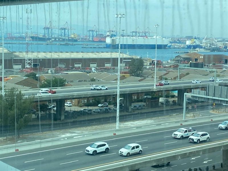An elevated view from an office window overlooking a highway, industrial port area, and shipping vessels.