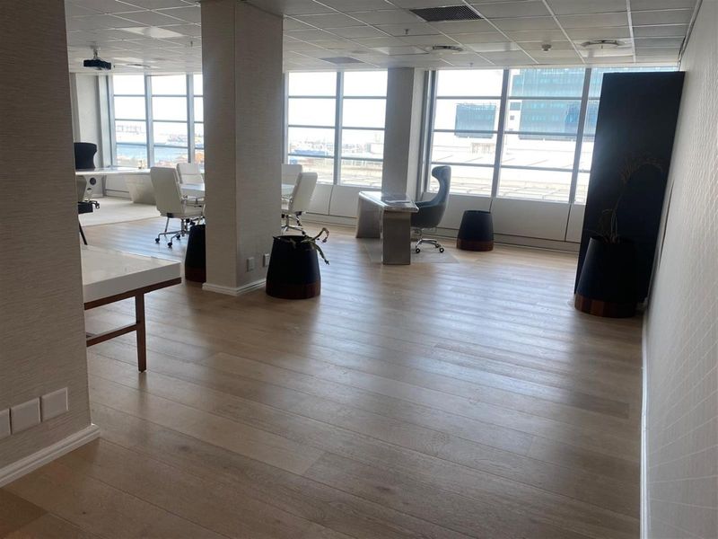 Modern open-plan office space featuring large windows with natural light, laminate flooring, and a professional suspended ceiling layout.