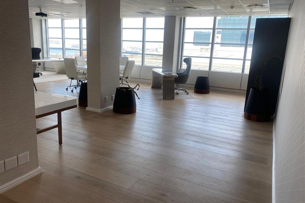 Modern open-plan office space featuring large windows with natural light, laminate flooring, and a professional suspended ceiling layout.