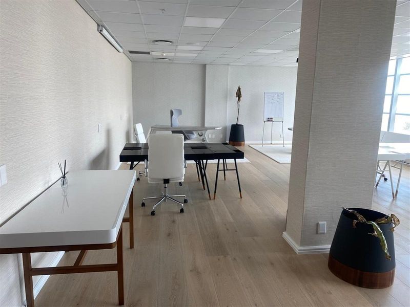 A bright, modern open-plan office space featuring light wood flooring, textured wall finishes, and a suspended ceiling with integrated lighting.