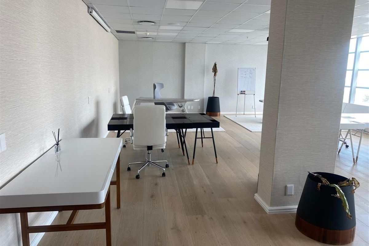 A bright, modern open-plan office space featuring light wood flooring, textured wall finishes, and a suspended ceiling with integrated lighting.