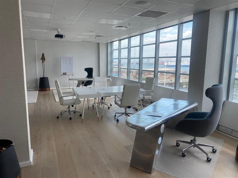 Modern office space featuring timber flooring, a suspended ceiling with integrated lighting, and expansive windows offering natural light and views.