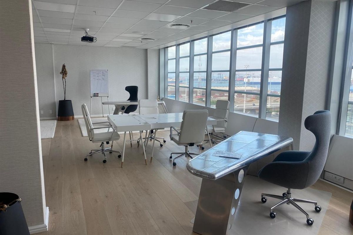 Modern office space featuring timber flooring, a suspended ceiling with integrated lighting, and expansive windows offering natural light and views.