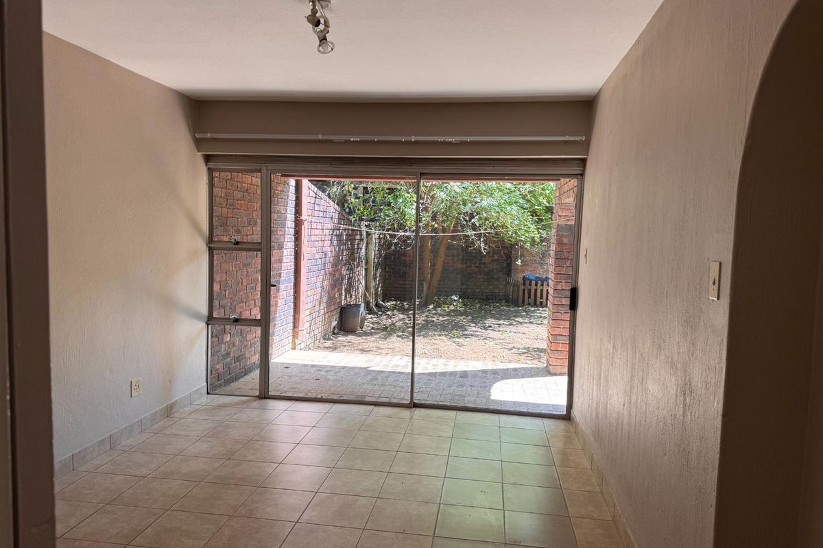 An empty living room featuring tiled flooring and a large sliding glass door that opens onto a private paved patio and garden area.