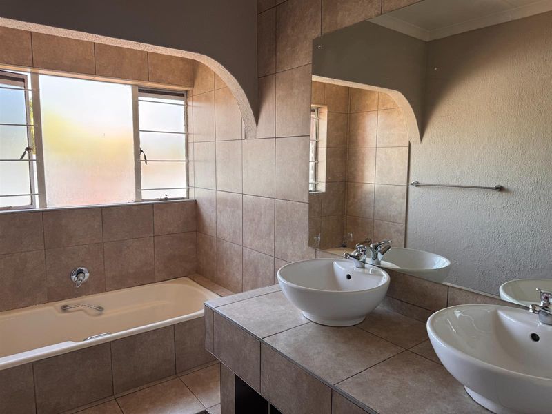 A functional bathroom featuring a built-in bathtub, double vanity with vessel sinks, and neutral wall tiling.