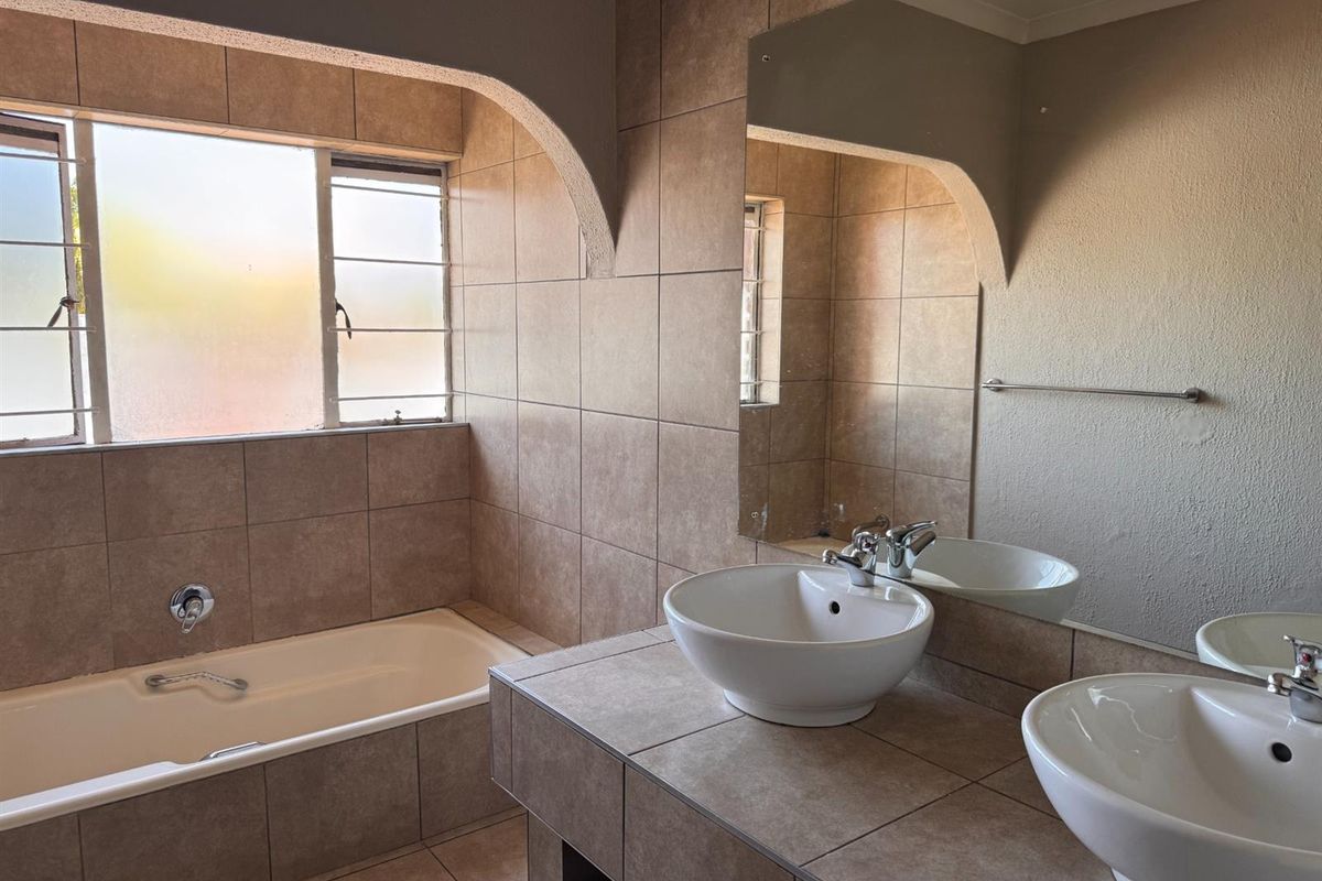 A functional bathroom featuring a built-in bathtub, double vanity with vessel sinks, and neutral wall tiling.