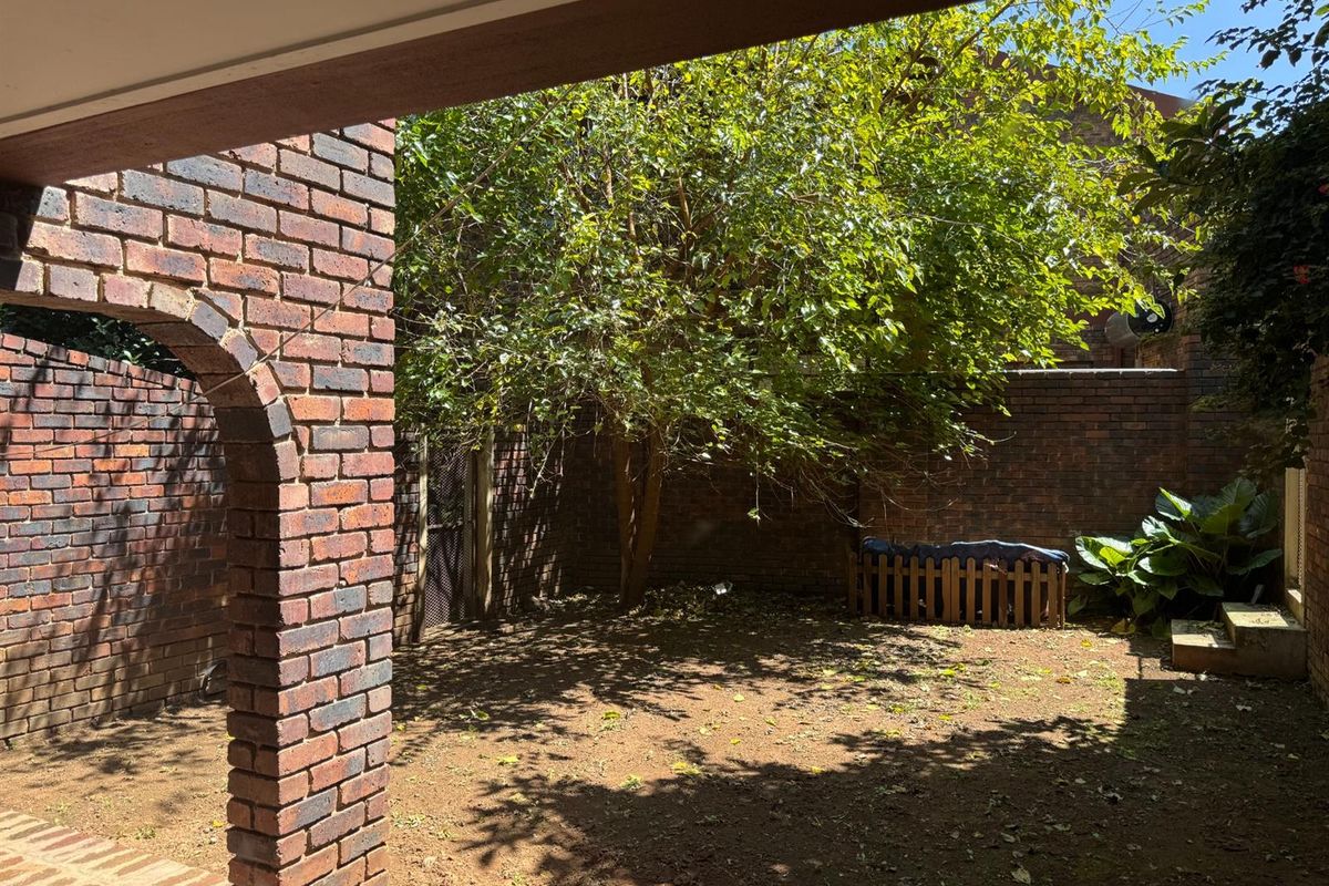 A private rear courtyard featuring a brick archway, paved patio space, and established garden area enclosed by brick boundary walls.