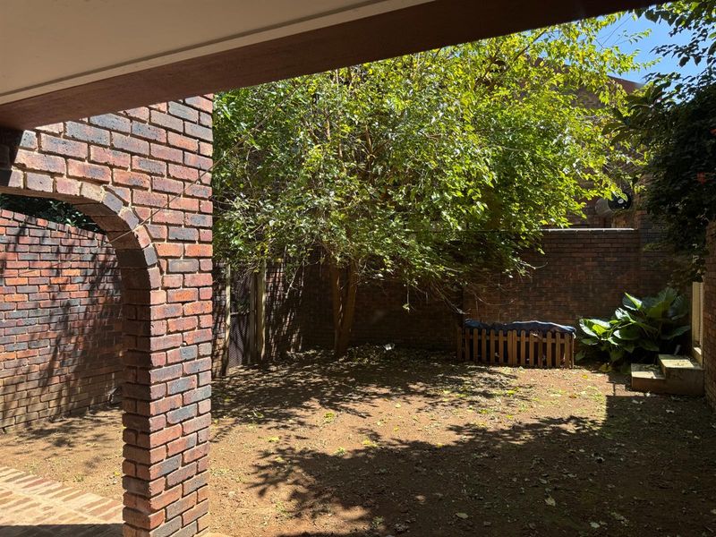 A private rear courtyard featuring a brick archway, paved patio space, and established garden area enclosed by brick boundary walls.