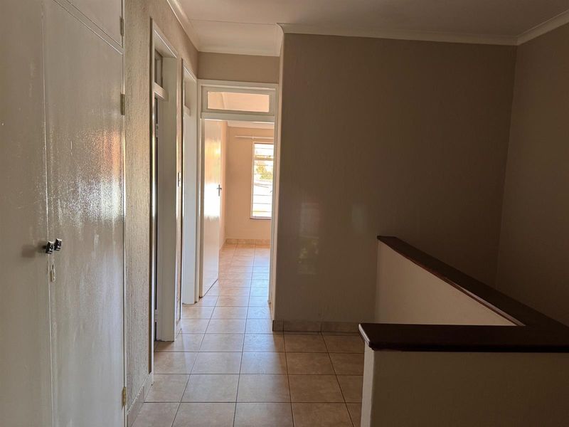 A bright, tiled hallway featuring a built-in cupboard and a staircase balustrade, leading towards a sunlit room at the end of the passage.