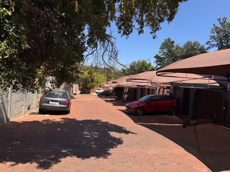 Exterior view of the townhouse complex driveway featuring brick paving, covered parking bays with shade cloth, and perimeter boundary walling.