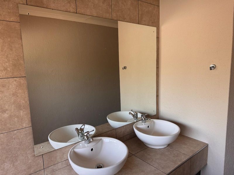 A bathroom vanity area featuring a tiled countertop with dual vessel sinks, chrome fixtures, and a large wall-mounted mirror.