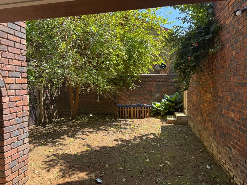 A private rear courtyard featuring high brick boundary walls, concrete steps, and a mature tree, offering potential for landscaping and outdoor living.