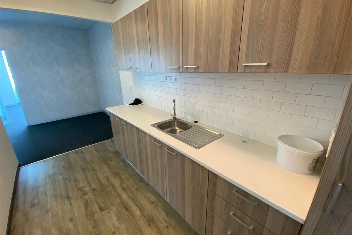 A modern office kitchenette featuring wood-grain cabinetry, a stainless steel sink, and a clean white subway tile backsplash.