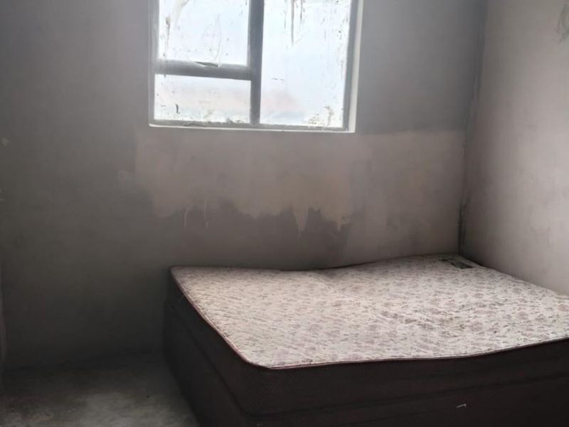 A bedroom in shell condition featuring unfinished plaster walls, exposed concrete flooring, and a window requiring repair.