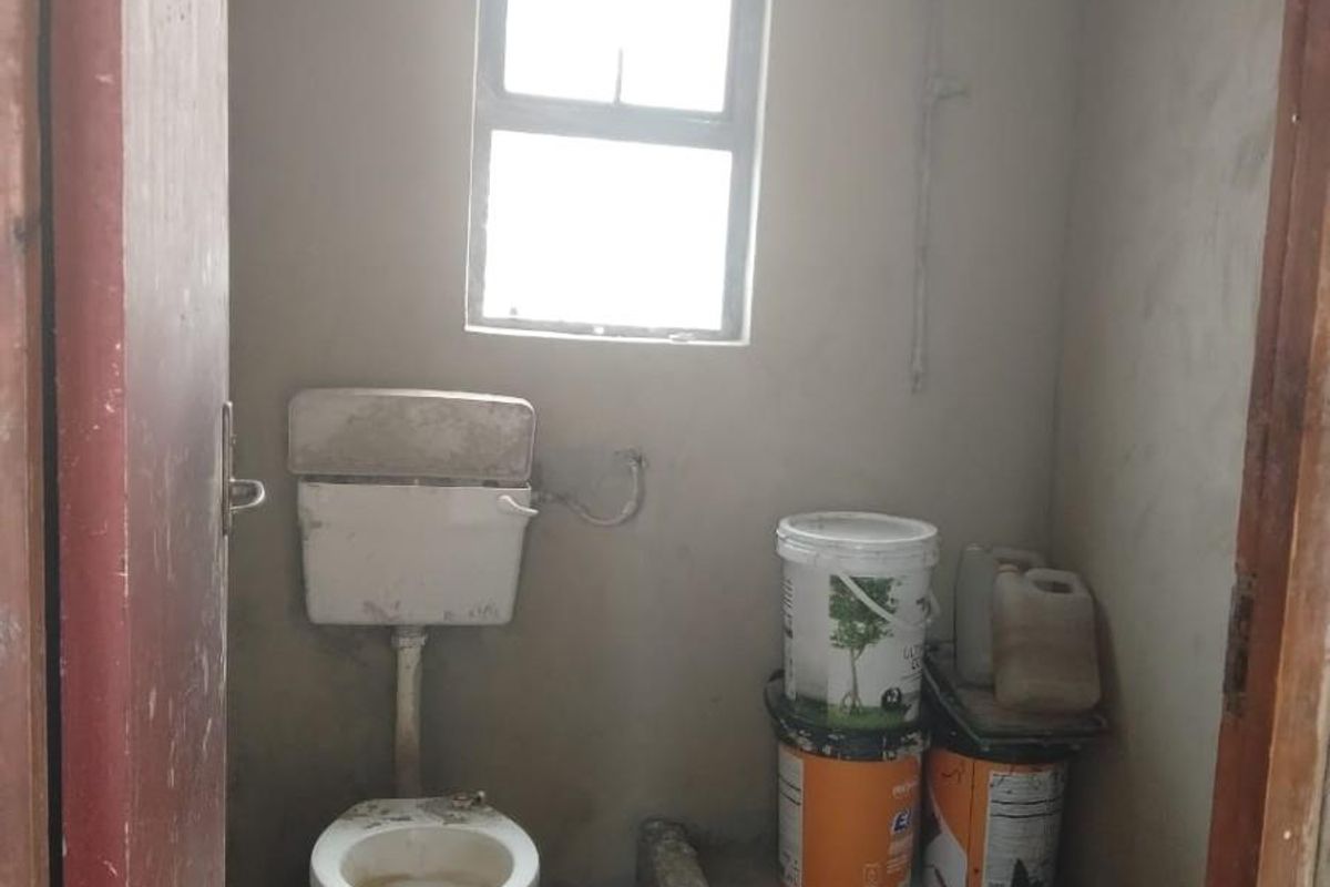 A small, unfinished bathroom featuring a toilet, raised shower base, and window, requiring significant renovation and finishing to reach a functional standard.