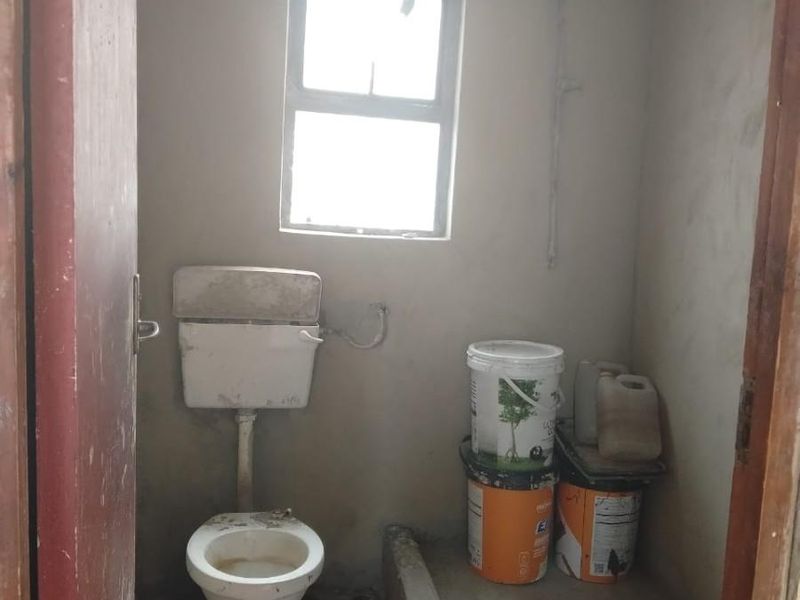 A small, unfinished bathroom featuring a toilet, raised shower base, and window, requiring significant renovation and finishing to reach a functional standard.