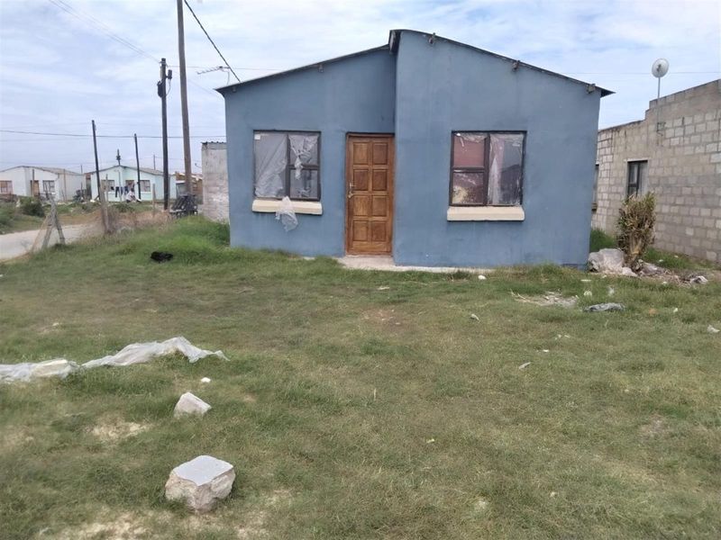 A detached single-story residential property featuring a blue painted exterior, timber entrance door, and metal-framed windows, situated on a grassed plot.