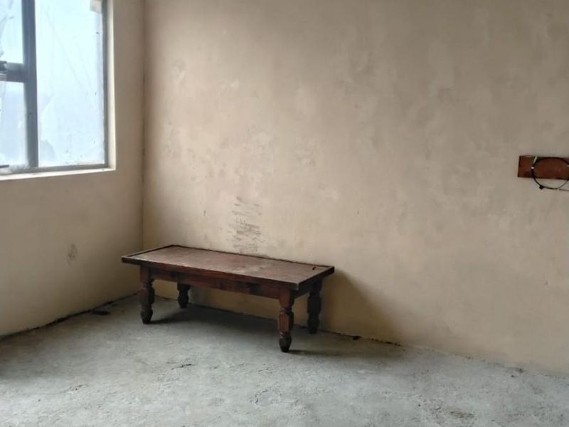 An unfinished bedroom space featuring raw concrete flooring, exposed ceiling beams, and unpainted plaster walls, offering a blank canvas for renovation.