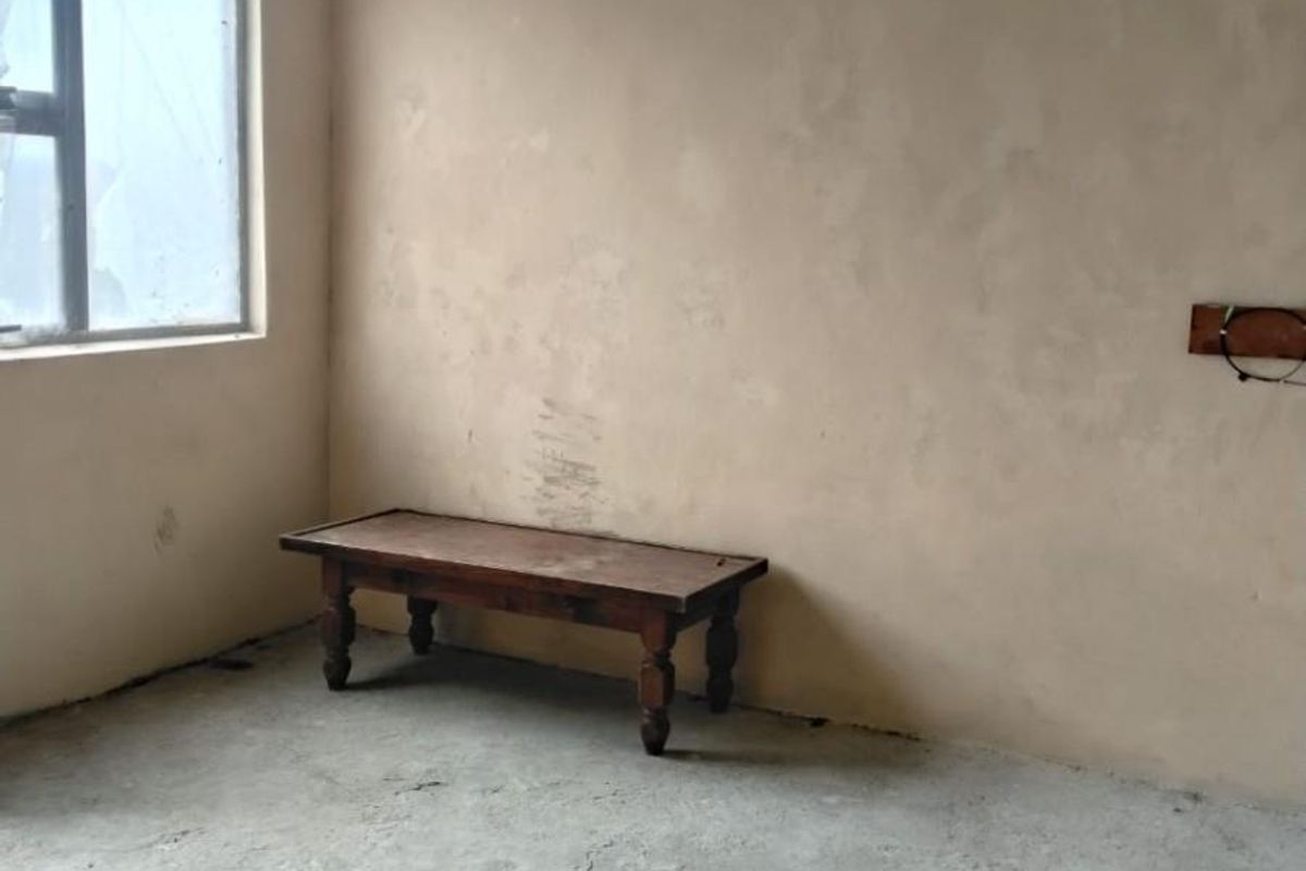An unfinished bedroom space featuring raw concrete flooring, exposed ceiling beams, and unpainted plaster walls, offering a blank canvas for renovation.