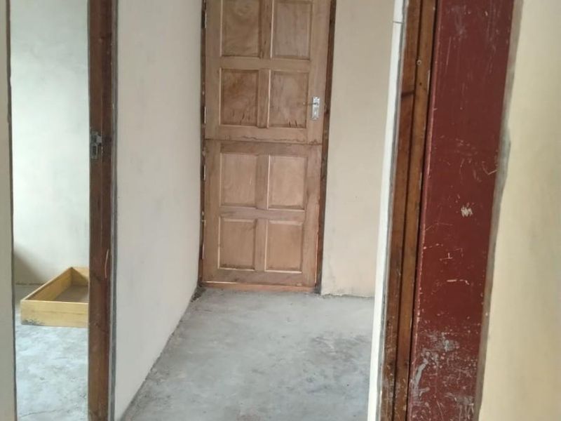 An unfinished interior hallway featuring exposed concrete ceilings, cement flooring, and timber panel doors, requiring cosmetic updates and finishing work.