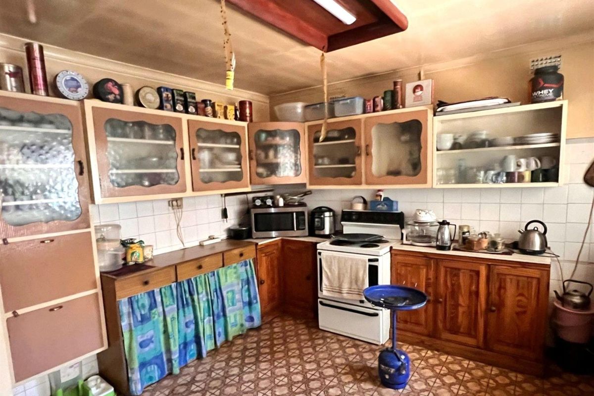 A dated kitchen featuring traditional wooden cabinetry, tiled splashbacks, and a freestanding stove, offering significant potential for a modern renovation.