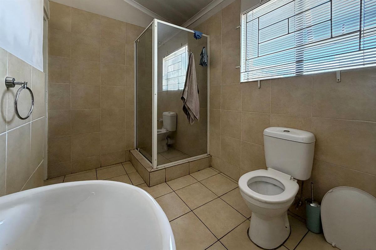 A functional bathroom featuring a corner shower enclosure, a standard toilet, and tiled flooring and walls throughout.