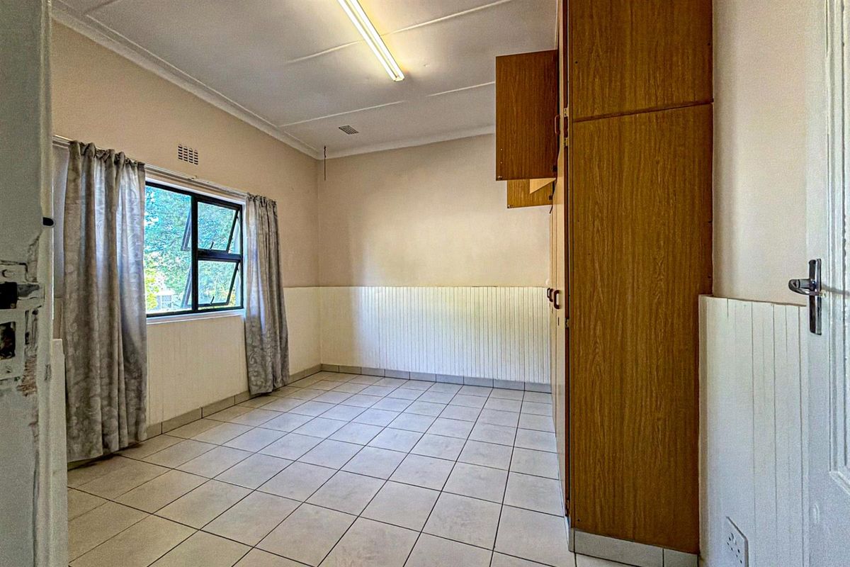 A functional bedroom featuring tiled flooring, built-in wooden cabinetry, and wall paneling, offering a neutral space ready for personalization.