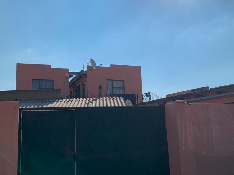 Front view of the property featuring a solid metal gate, boundary wall, and corrugated roofing under a clear sky.