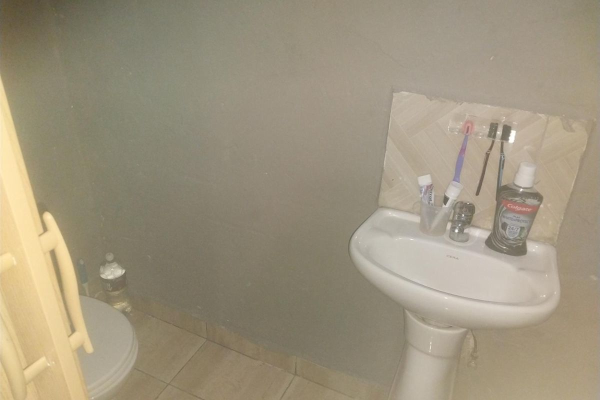 A compact bathroom featuring a white pedestal basin with a tiled splashback and a standard toilet.