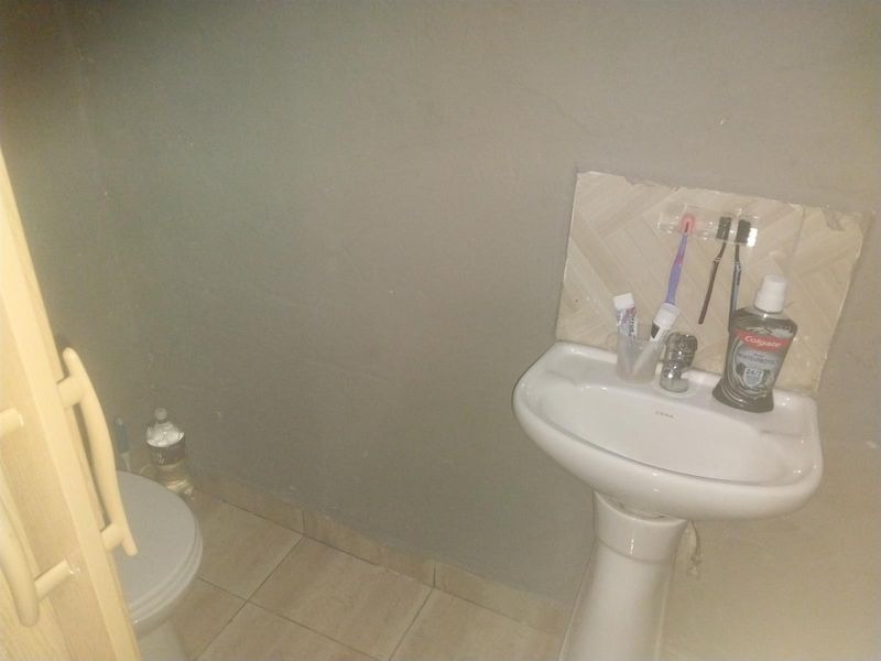 A compact bathroom featuring a white pedestal basin with a tiled splashback and a standard toilet.