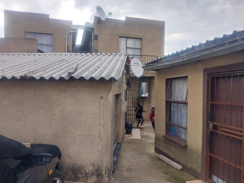 Rear exterior view of the property showing multiple structures with weathered plaster finishes, corrugated roofing, and security features.