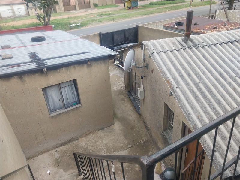 Elevated view of a rear courtyard area featuring corrugated and asbestos roofing, concrete paving, and a metal staircase.