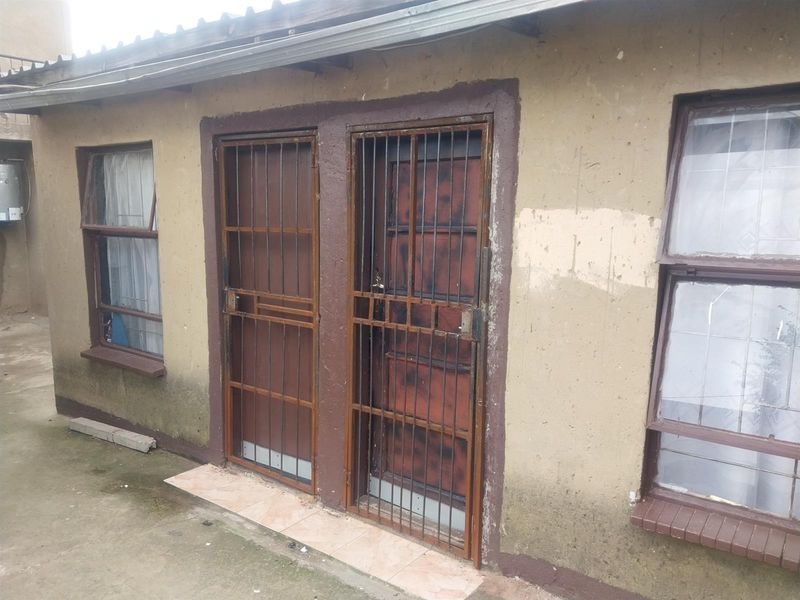 Exterior view of the rear building facade featuring security gates and steel window frames, showing signs of significant wear and weathering.